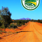Australian Owned certified business logo on photo of gravel road leading to Kata Tjuta in central Australia